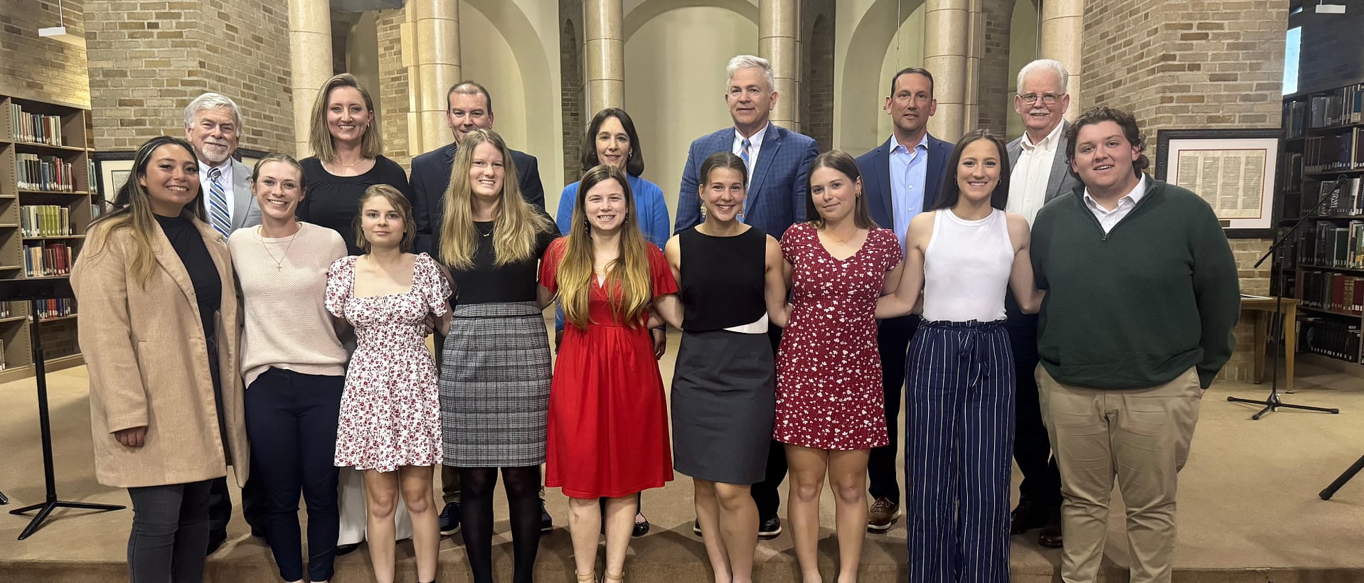 nine student-athletes stand in row with presenters in library