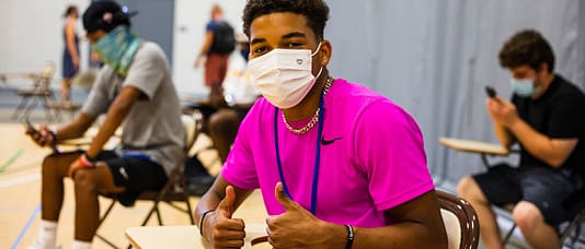 Student with mask on smiling with two thumbs up